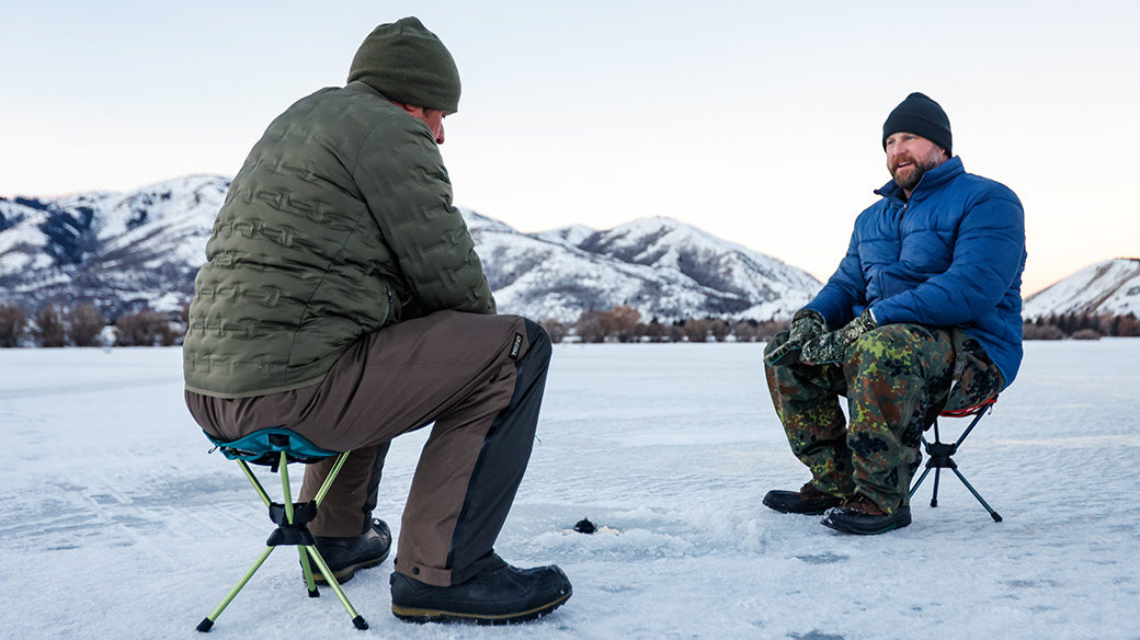Two men ice fishing with the compass 360 stool with a beautiful mountainscape background