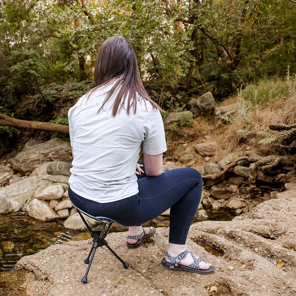Person sitting on a portable stool by a stream in a forest