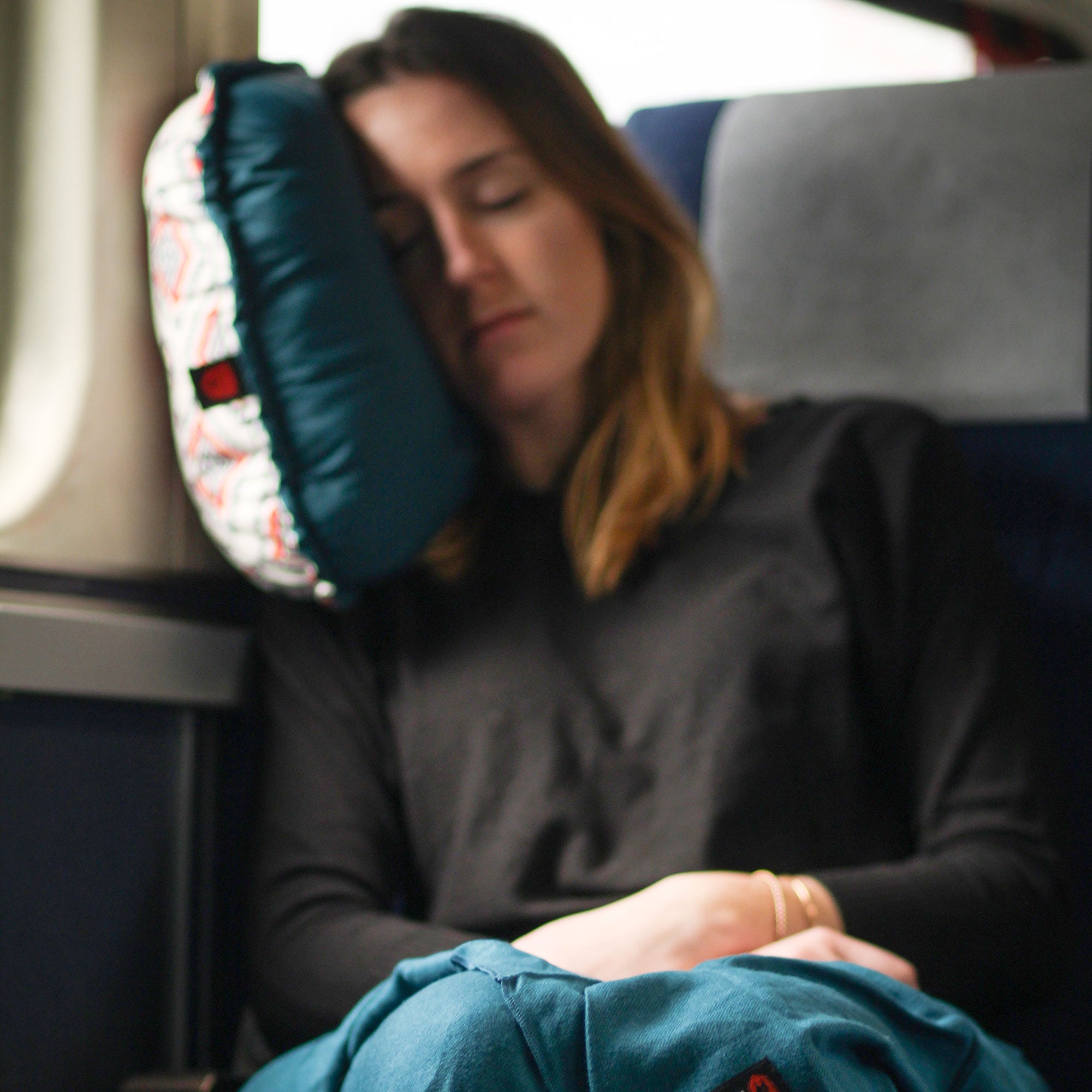 woman rests on the travel pillow inside of an airplane on the window seat