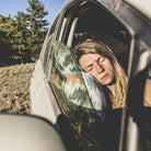 travel pillow in a car window as a woman rests her head on the side of it sleeping soundly