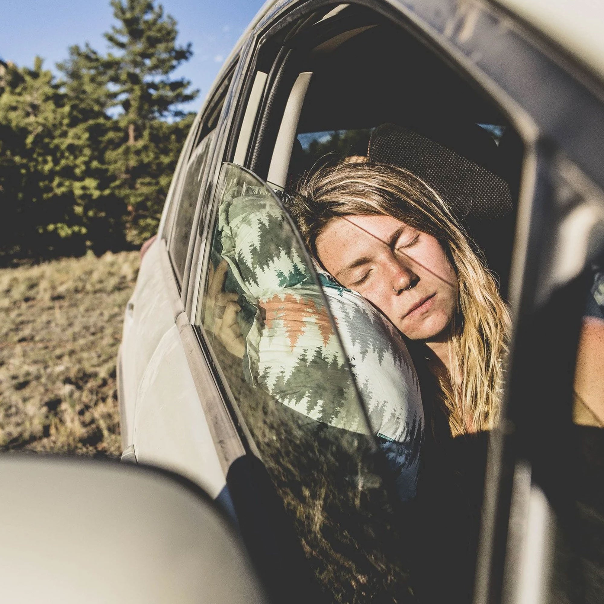 travel pillow in a car window as a woman rests her head on the side of it sleeping soundly
