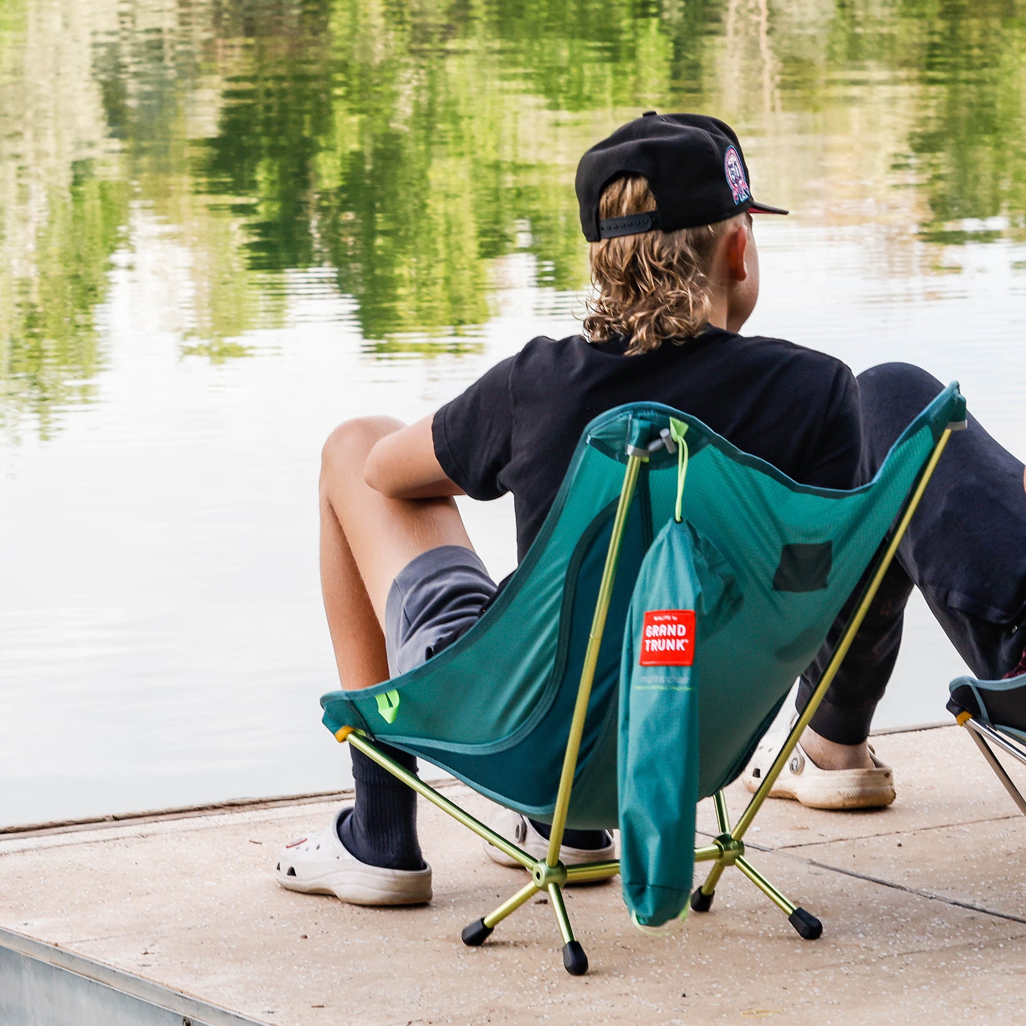 Young man sits in mantis chair on a dock by a lake fishing