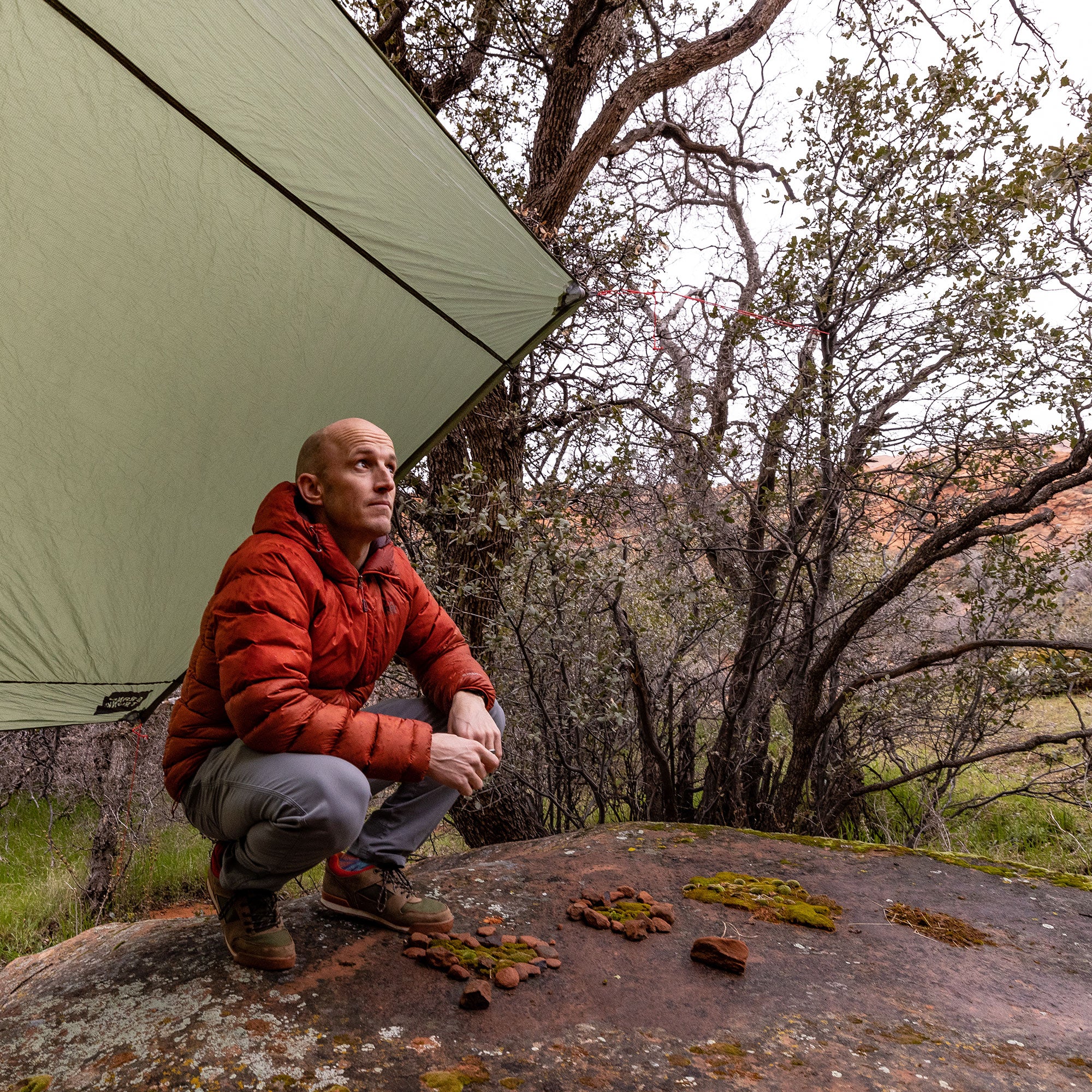 man crouches underneath the moab to stay dry in a rocky desert forest area