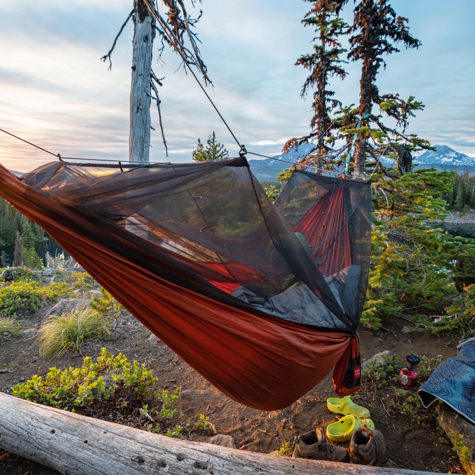 skeeter beeter hammock with integrated bug net in the forest with some crocs underneath and mountains in the background