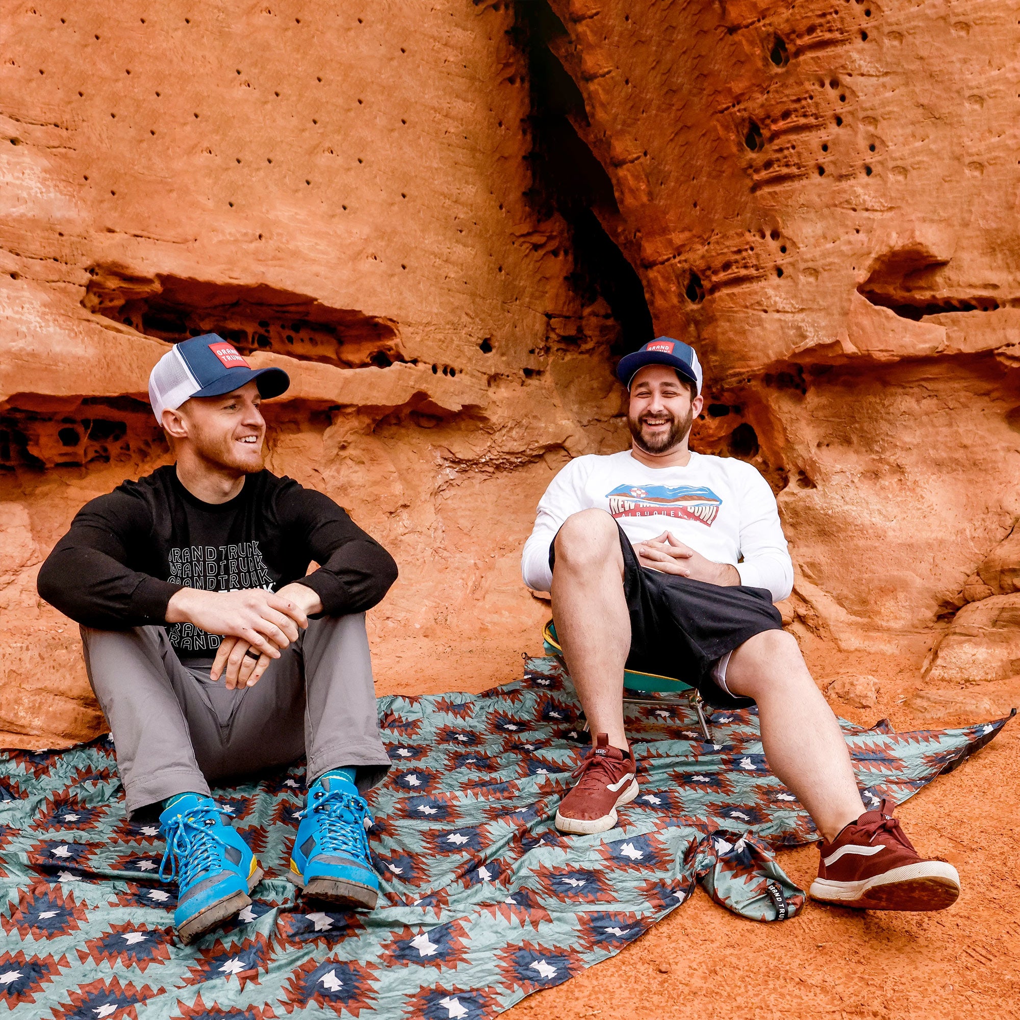 Two men sit on adventure sheet in redstone desert area one with mantis chair dry safe and happy