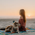 woman sits on adventure sheet on the beach with dog and klean kanteen waterbottle sunset showing a little shoulder