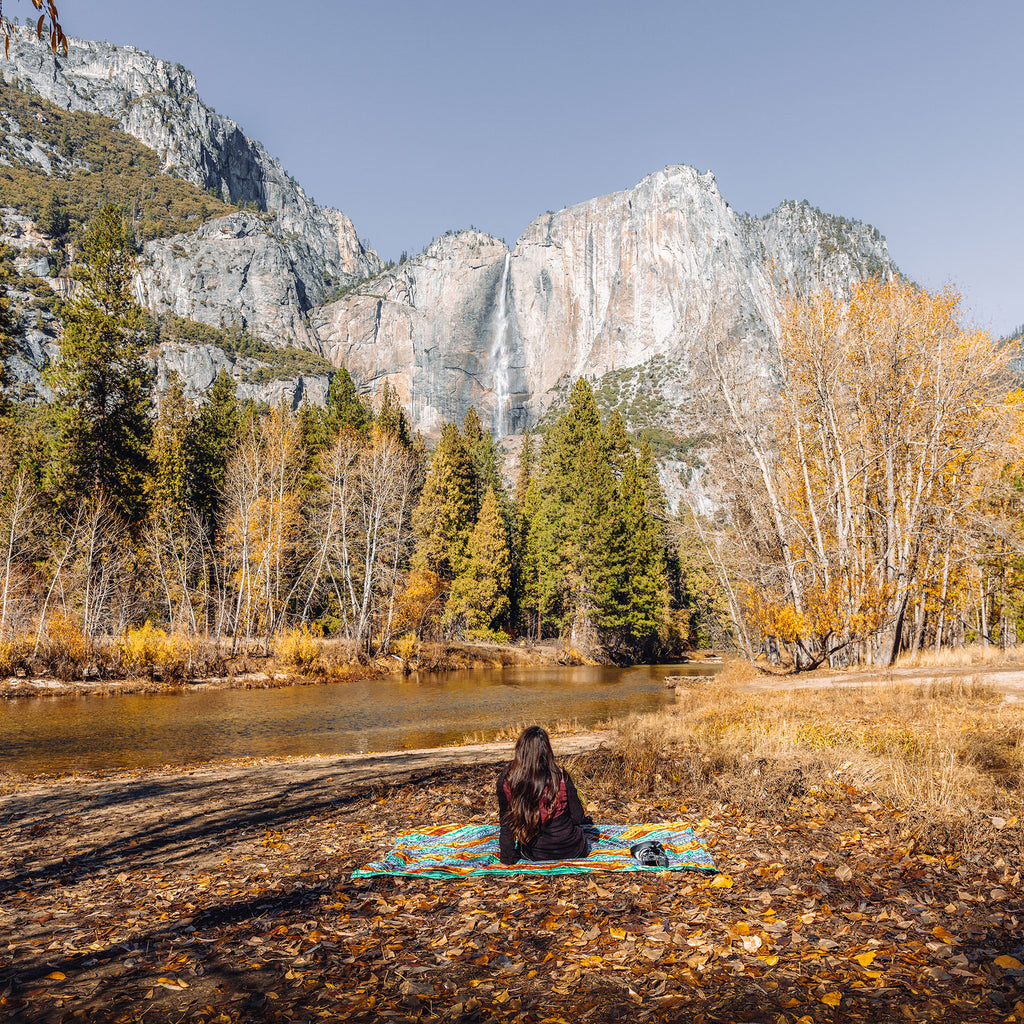 woman sits on adventure sheet hanging out in the fall foliage near a creek by the mountainside beautiful landscape