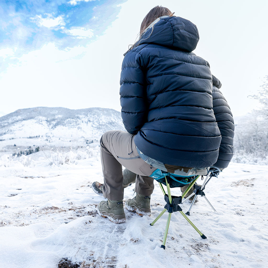 Young woman sitting on Grand Trunk Compass 360 Stool enjoying the view of a snowy mountain