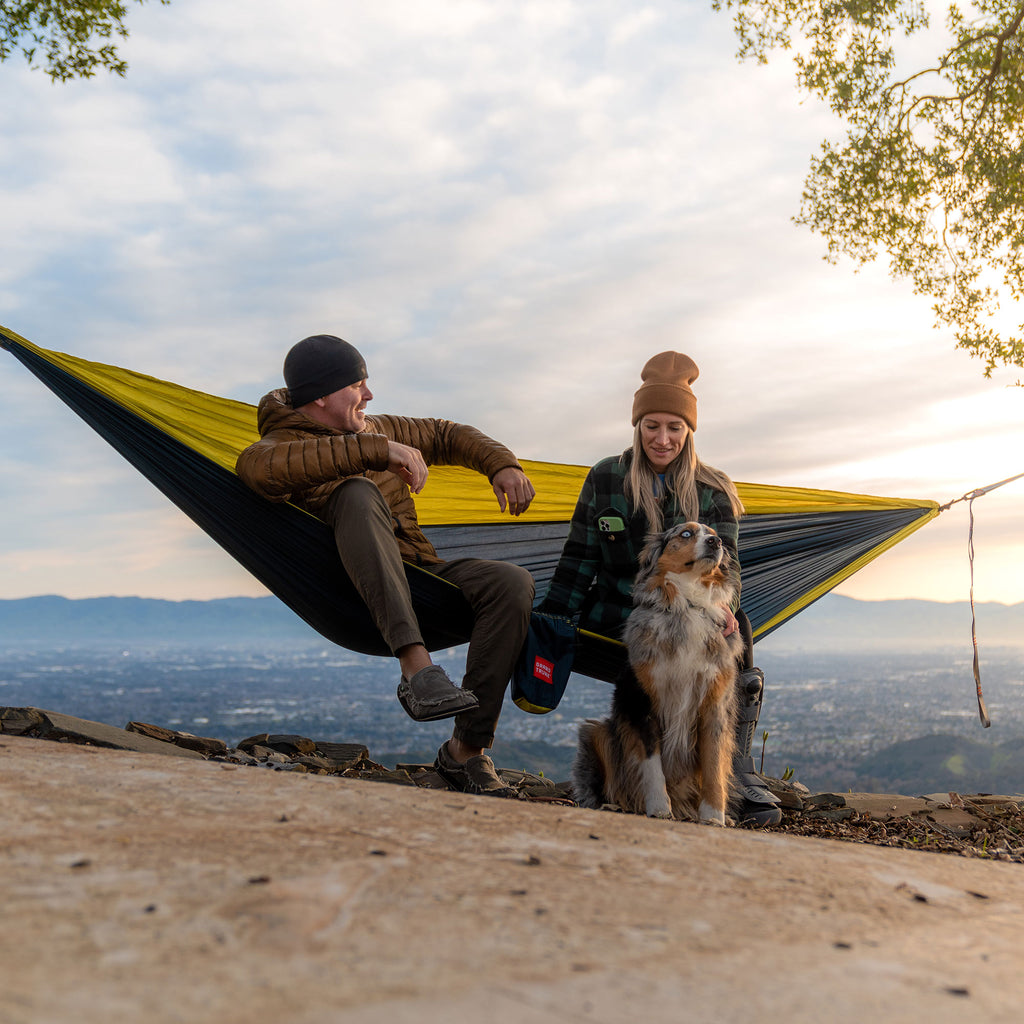 double deluxe hammock navy chartreuse man woman dog with cityscape and mountains in the background during golden hour