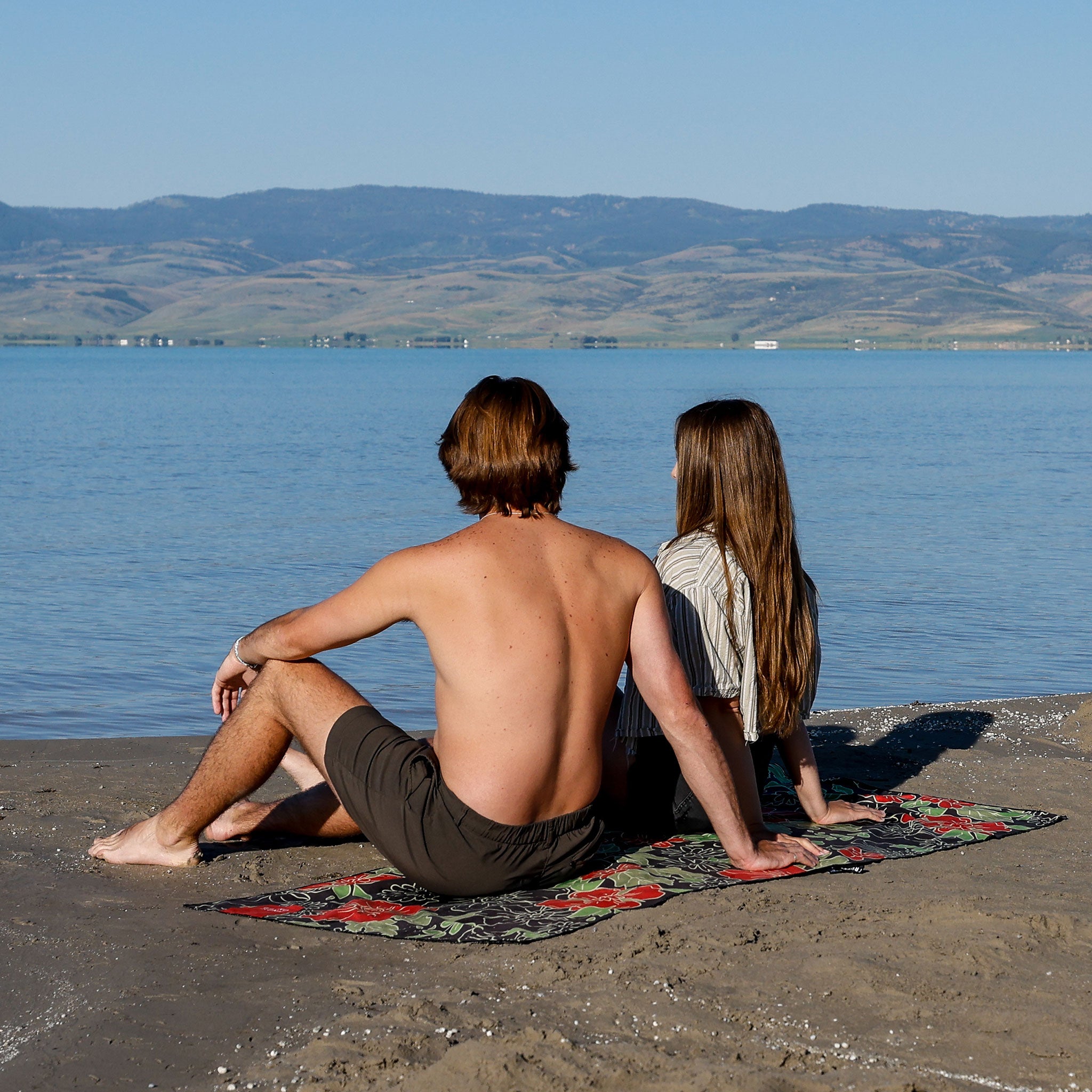 couple sitting on microfiber towel on lakefront beach