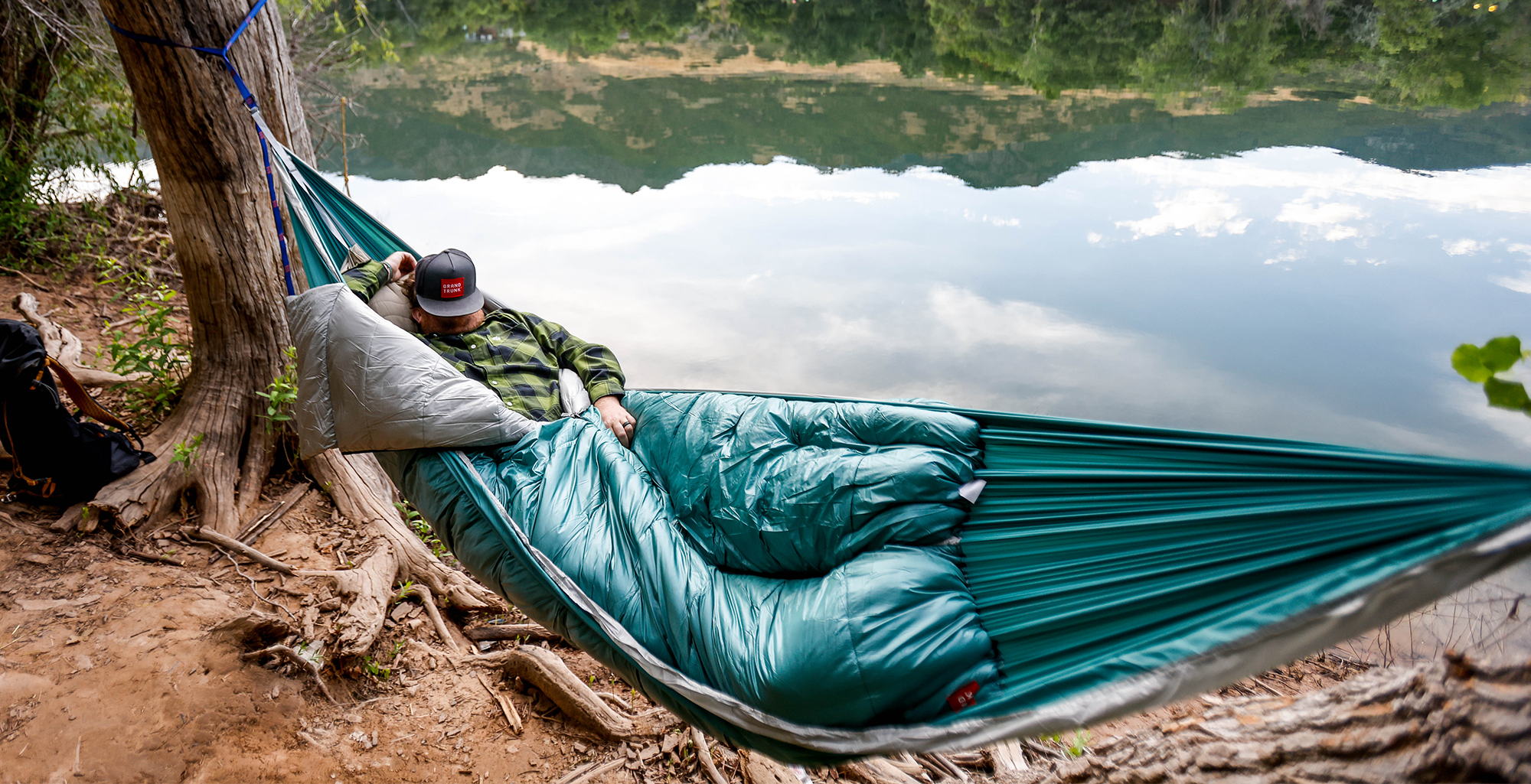 man sleeping in the evolution hammock next to lake