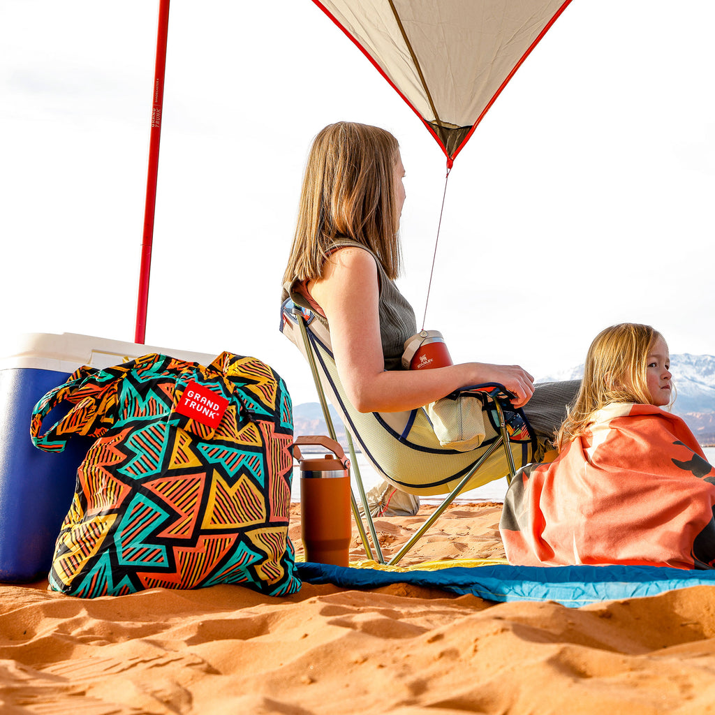 eco tote bag on a soft sand beach next to cooler and stanley mug under shadecaster with parasheet and microfiber towels and stonefly chair