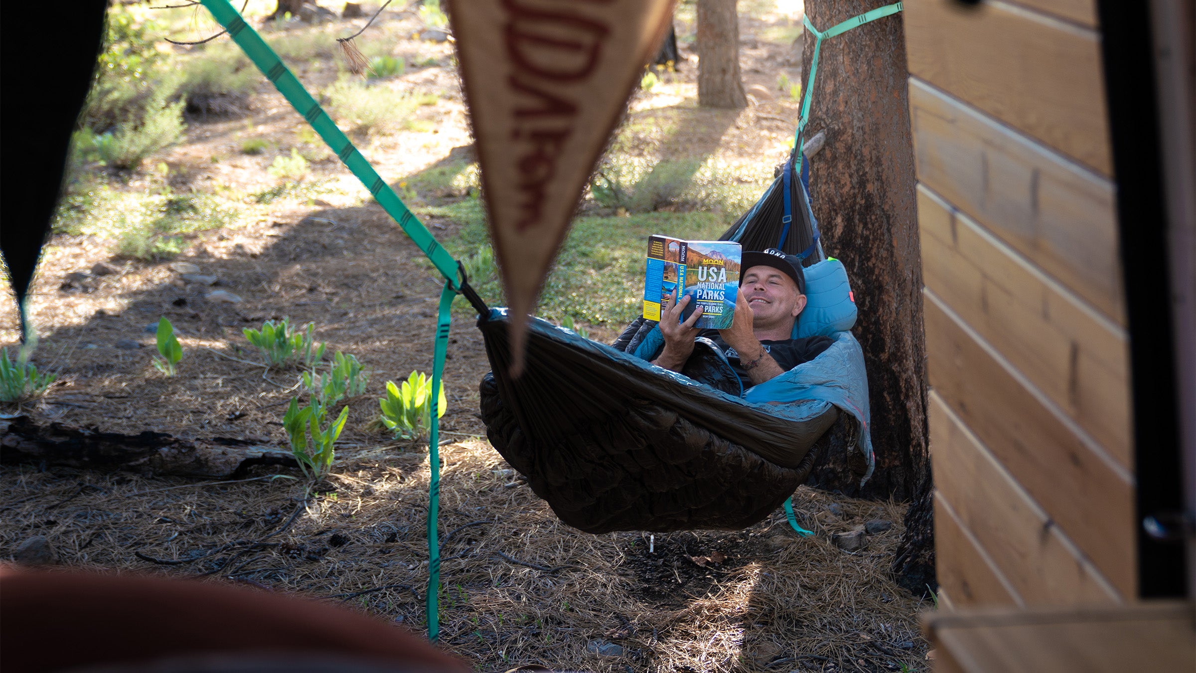 man lays in evolution 20 hammock reading happily with siesta pillow and trunk straps in forest