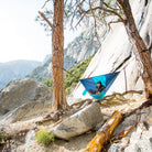 Woman relaxing in Grand Trunk ROVR hanging chair on a cliff face with mountains in the background