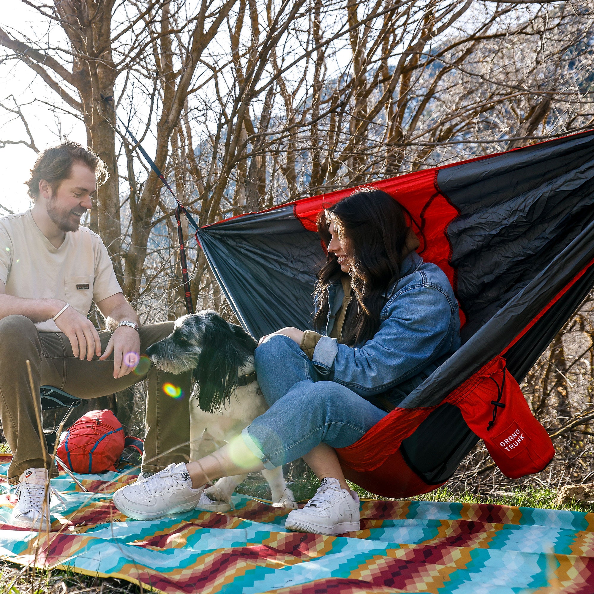Couple with dog relaxing in ROVR hanging Chair smiling laughing enjoying company with meadow mat underneath them