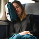 woman rests on the travel pillow inside of an airplane on the window seat