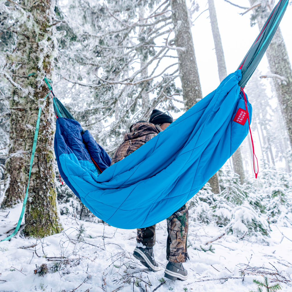 woman sits in a hammock with the thermaquilt wearing camouflage in a snowy forest