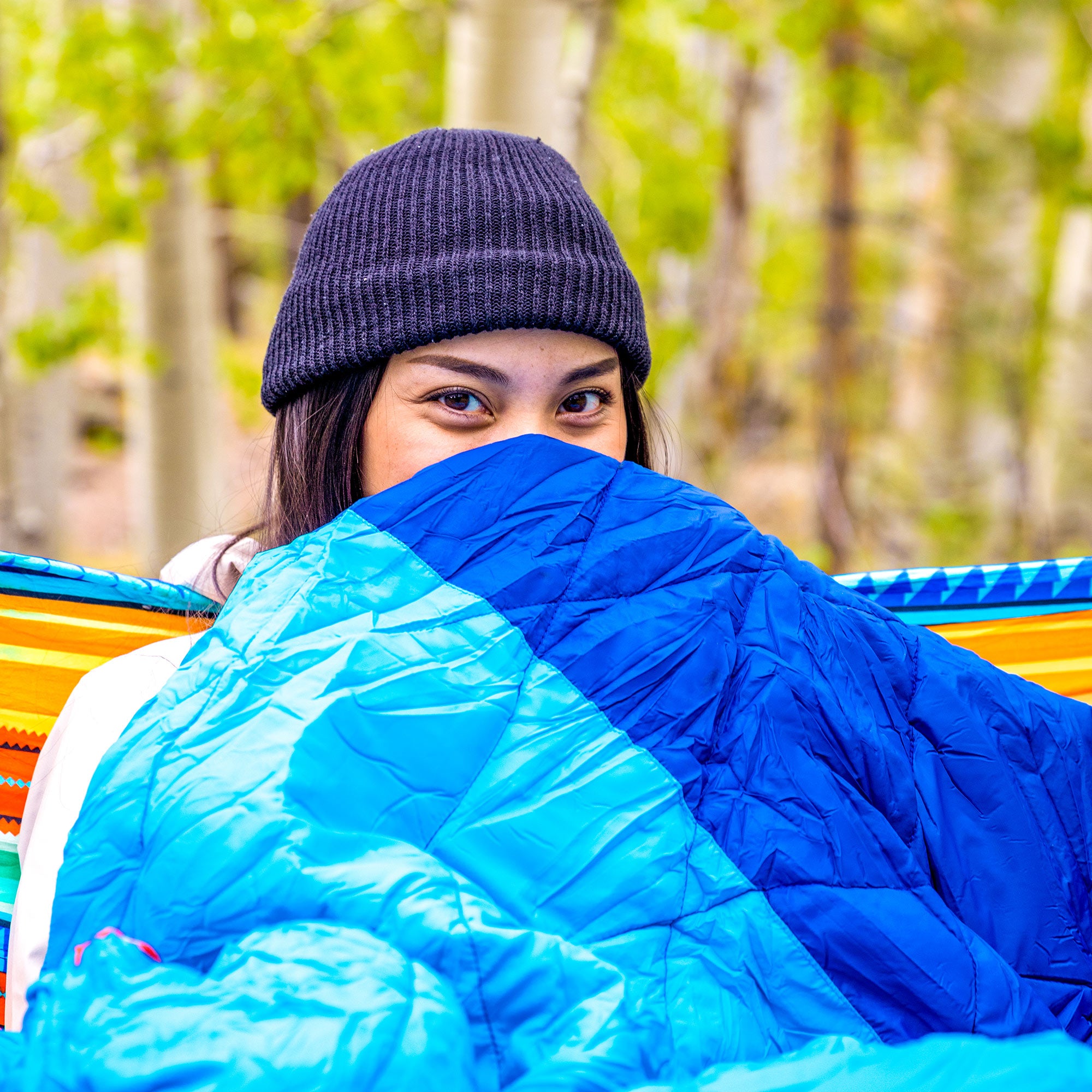 woman bundled up in the thermaquilt sitting in a hammock outside in a forest
