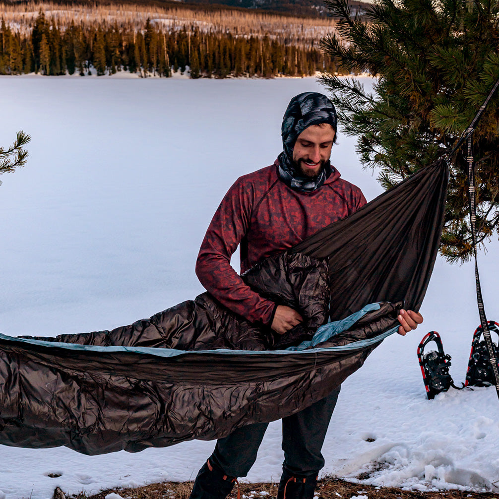 man setting up the evolution 20 hammock after snowshoeing to forest location