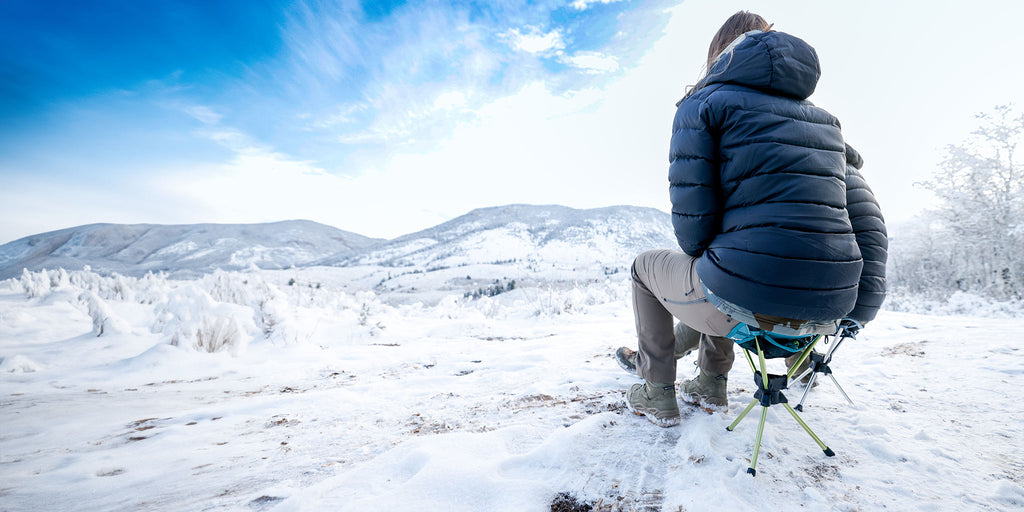 Young woman sitting on Grand Trunk Compass 360 Stool enjoying the view of a snowy mountain