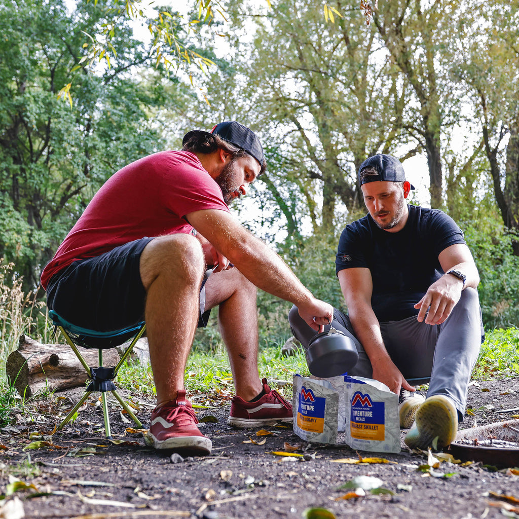 men in the woods camping and cooking backpacking meals while sitting on the compass 360° stool