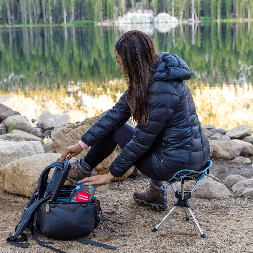 Woman sits on compass 360 stool and reaches into her pack for gear maybe camera photography bag