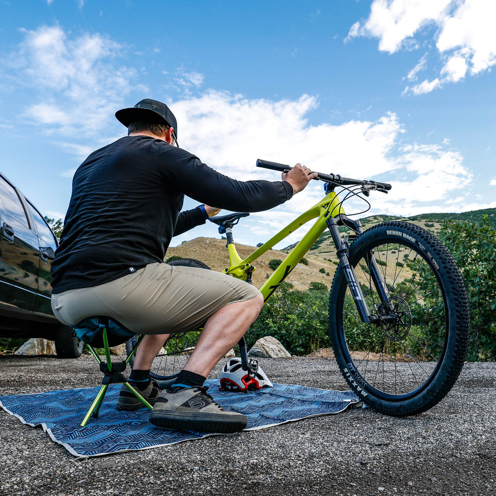 man fixes mountain bike while sitting on the compass 360 stool and meadow mat before hitting the trail