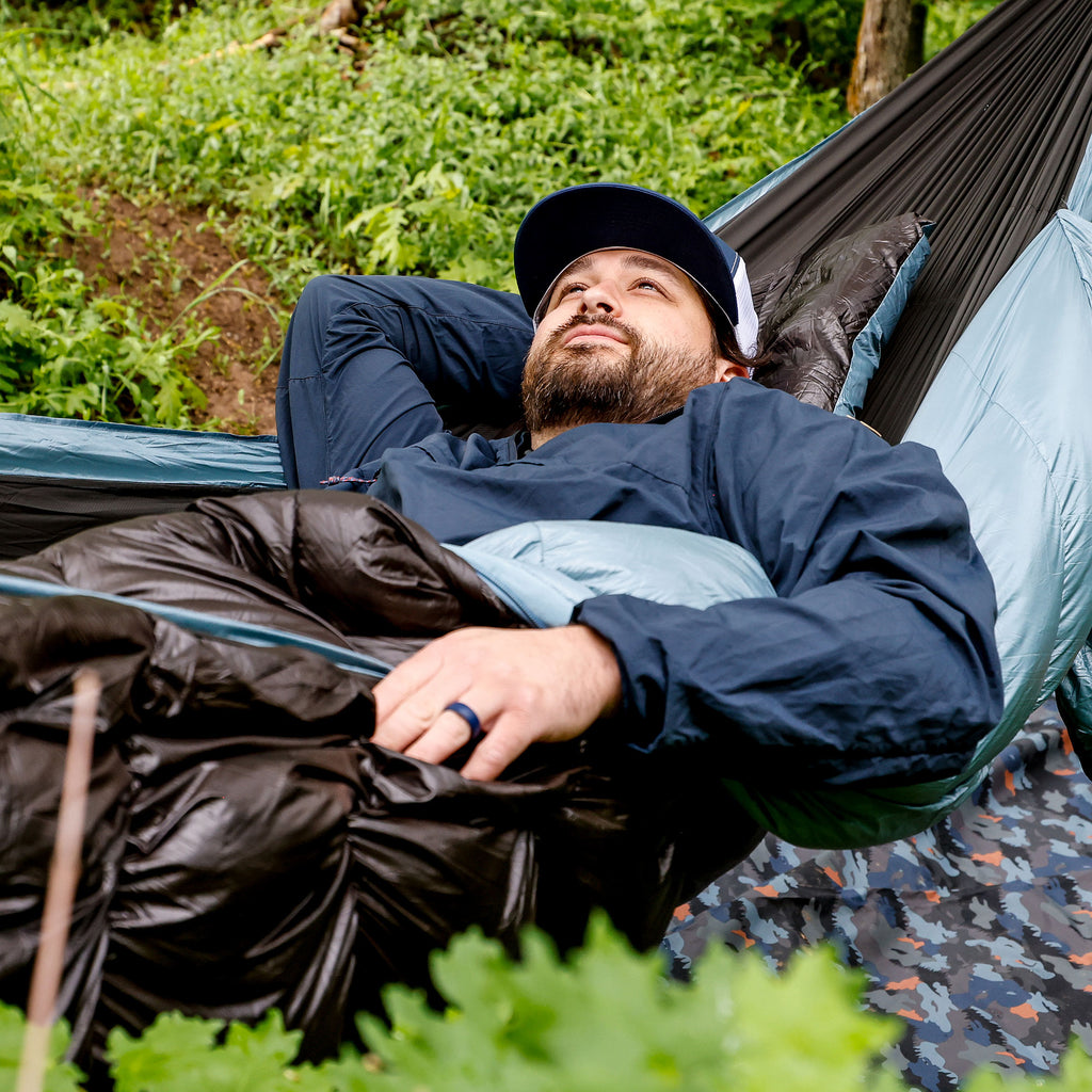 Man waking up in Evolution Hammock comfortable warm with meadow mat in background in forest green foliage