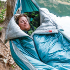 Man Sleeping comfortably and warm in Grand Trunk Evolution Synthetic sleeping bag Hammock next to lake