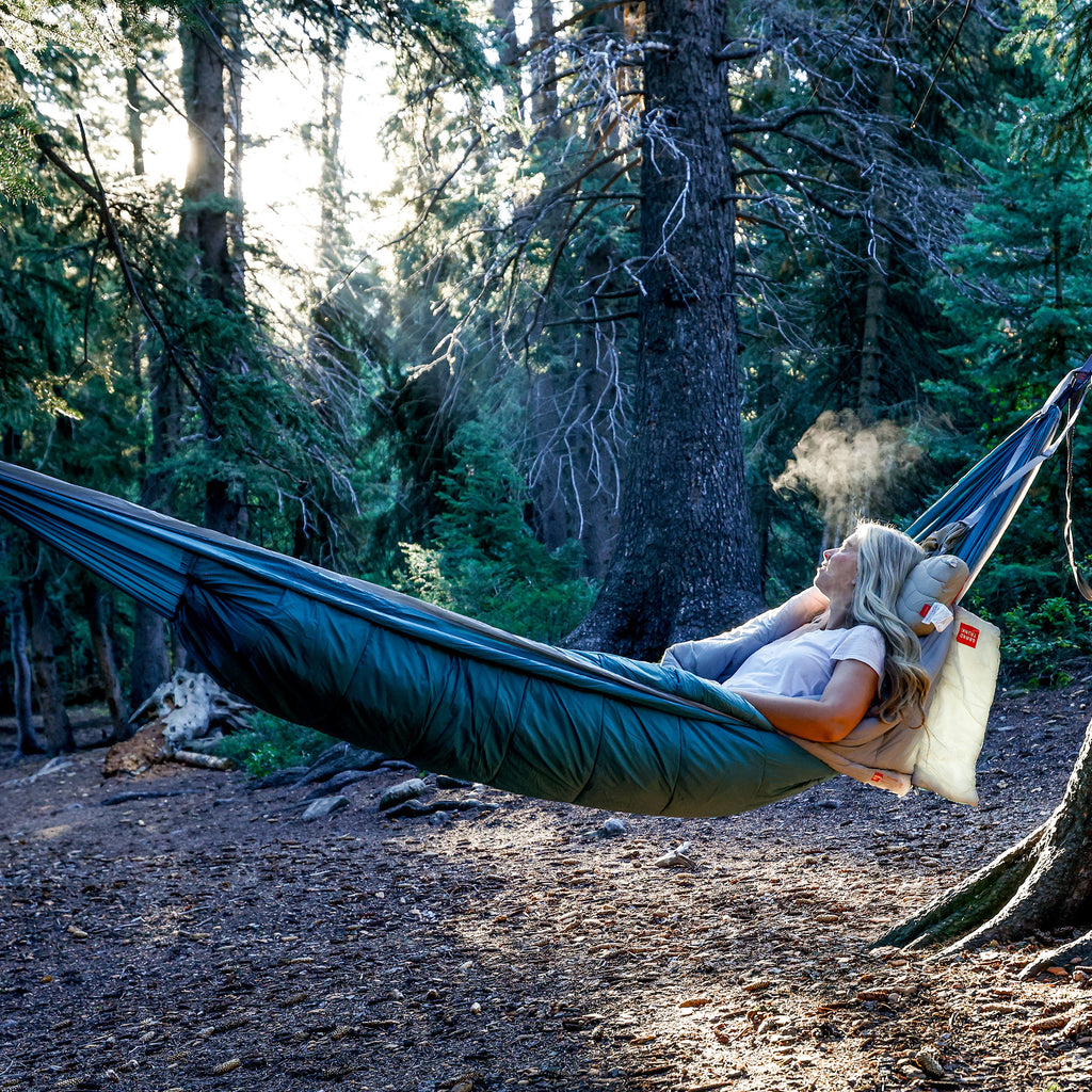 Woman laying in Grand Trunk Evolution Hammock staying warm and comfortable on a cool morning in the forest.