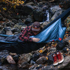 Man in Grand Trunk Evolution Hammock over riverbed waterfall in background fall camping foliage