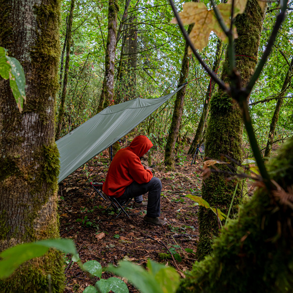 man finds shelter underneath the moab to stay dry in a rainy forest