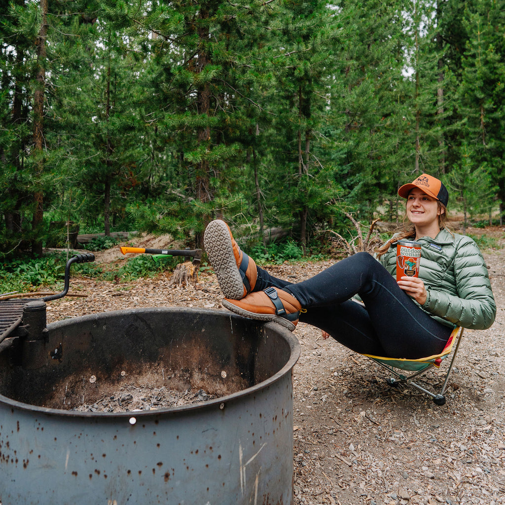 Woman at campground in Monarch Chair rocking and resting her feet up on firepit ring