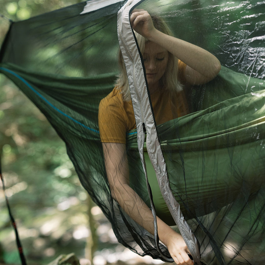 Mozzy bug net with woman inside hammock while zipping up j-zipper