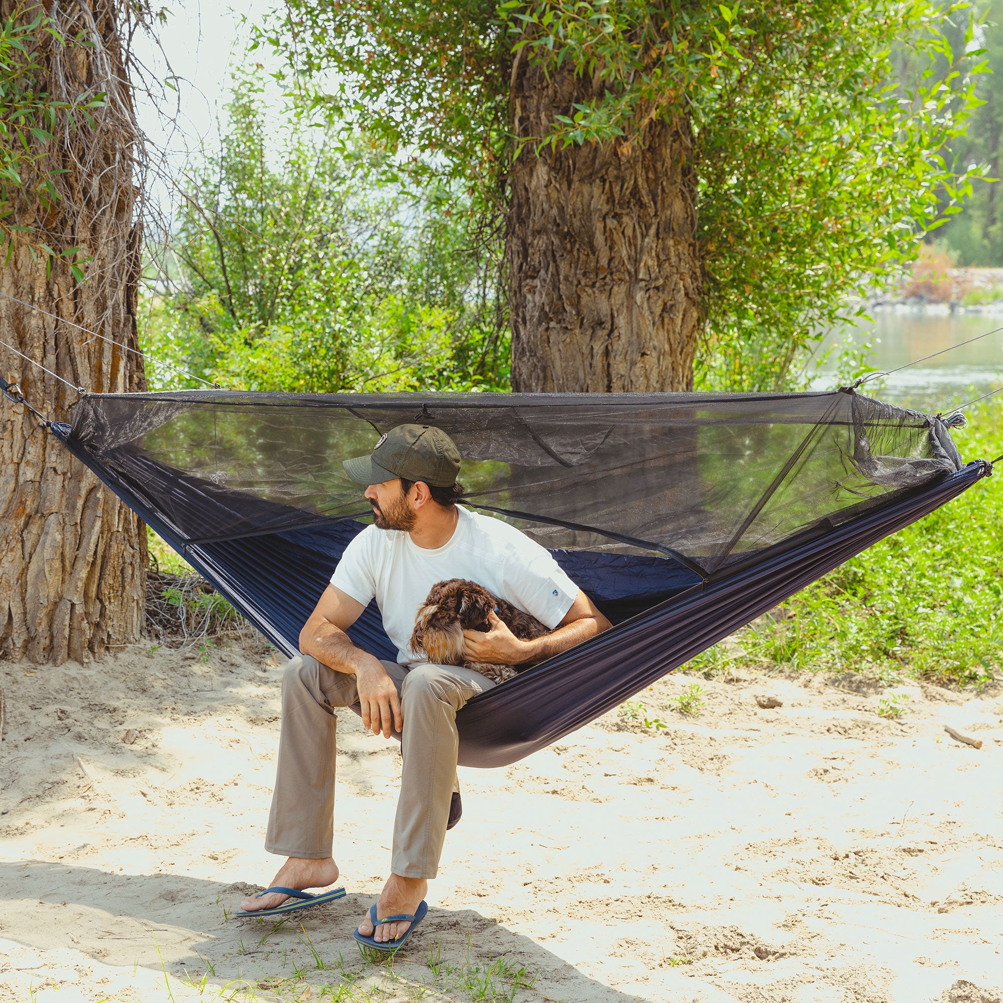man sits relaxed with his dog in the skeeter beeter hammock