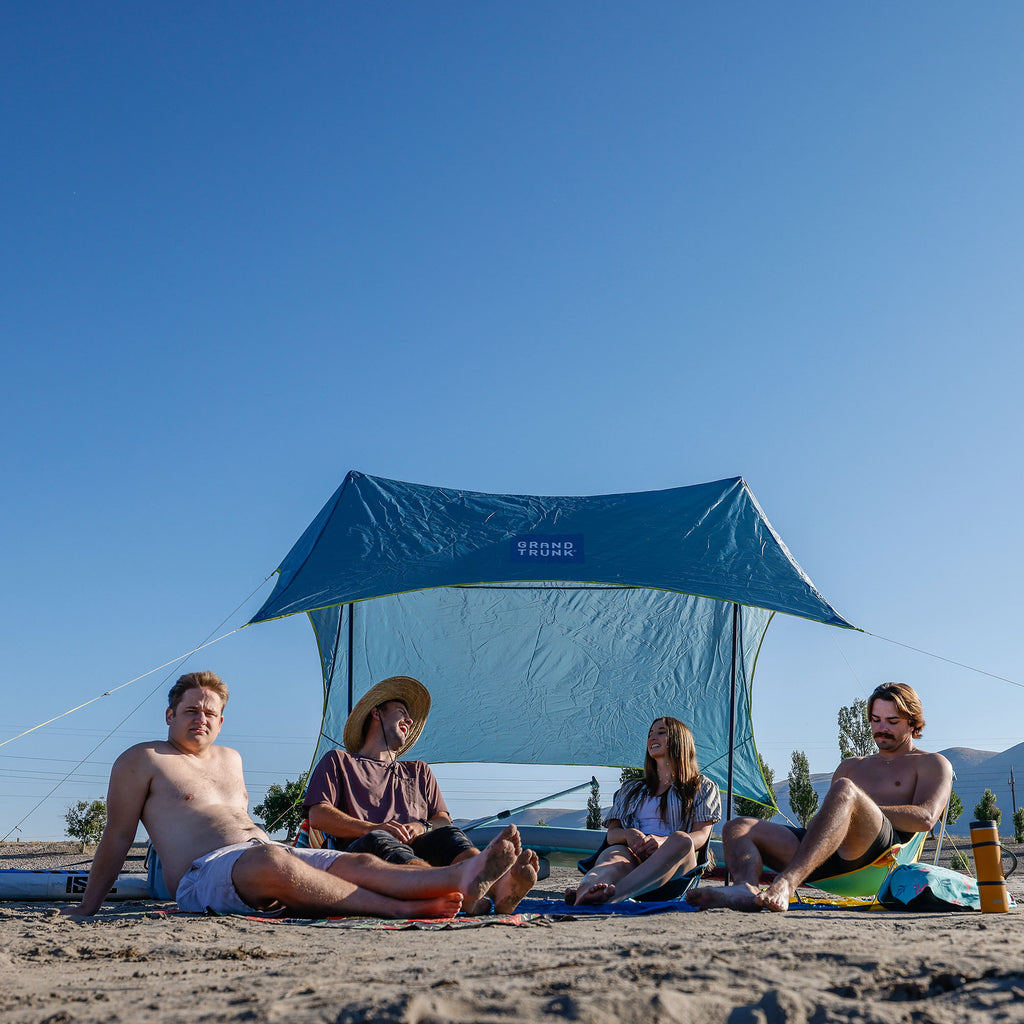 group hanging out under the shadecaster 4 on the beach with a parasheet, mayfly chairs, and microfiber towels