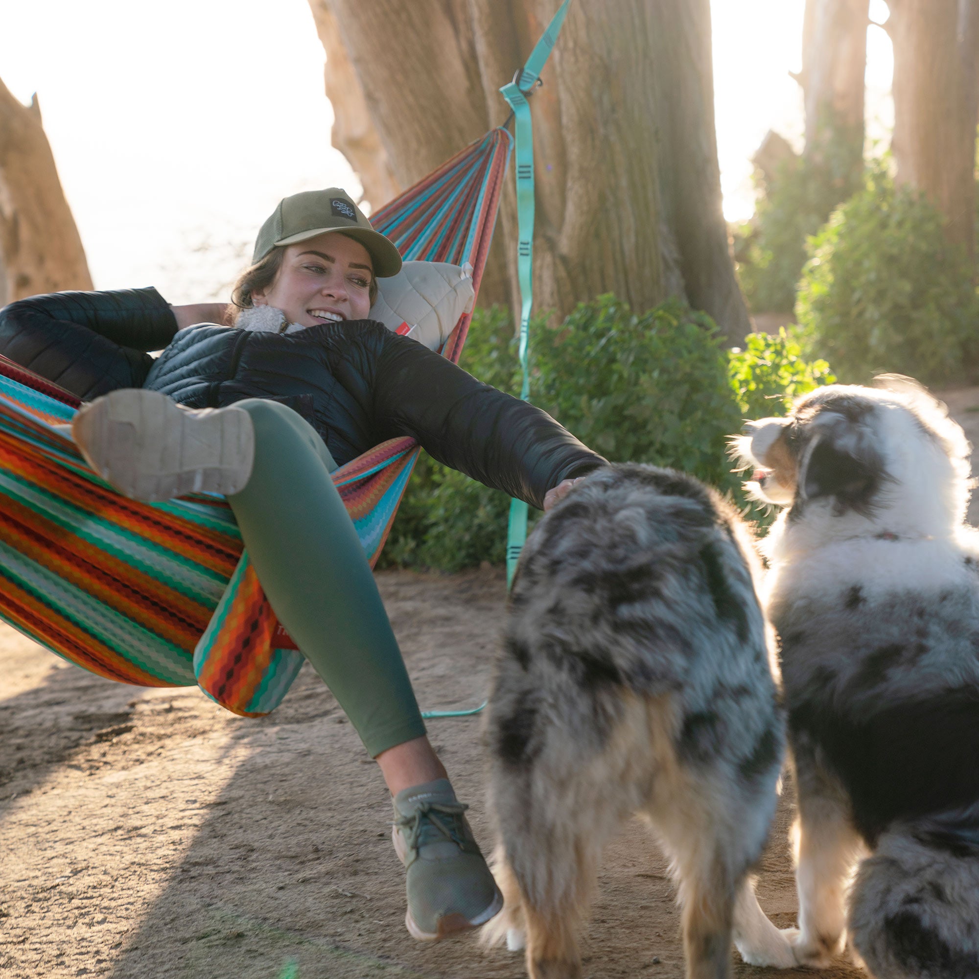Woman resting in hammock with Grand Trunk siesta hammock pillow petting her dogs in the forest