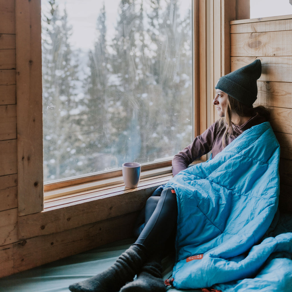 Woman looking out window while cuddled up in Grand Trunk Thermaquilt